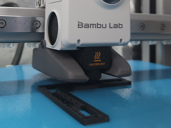 Cabeçote de impressora 3D sobre a mesa, imprimindo uma peça em filamento preto